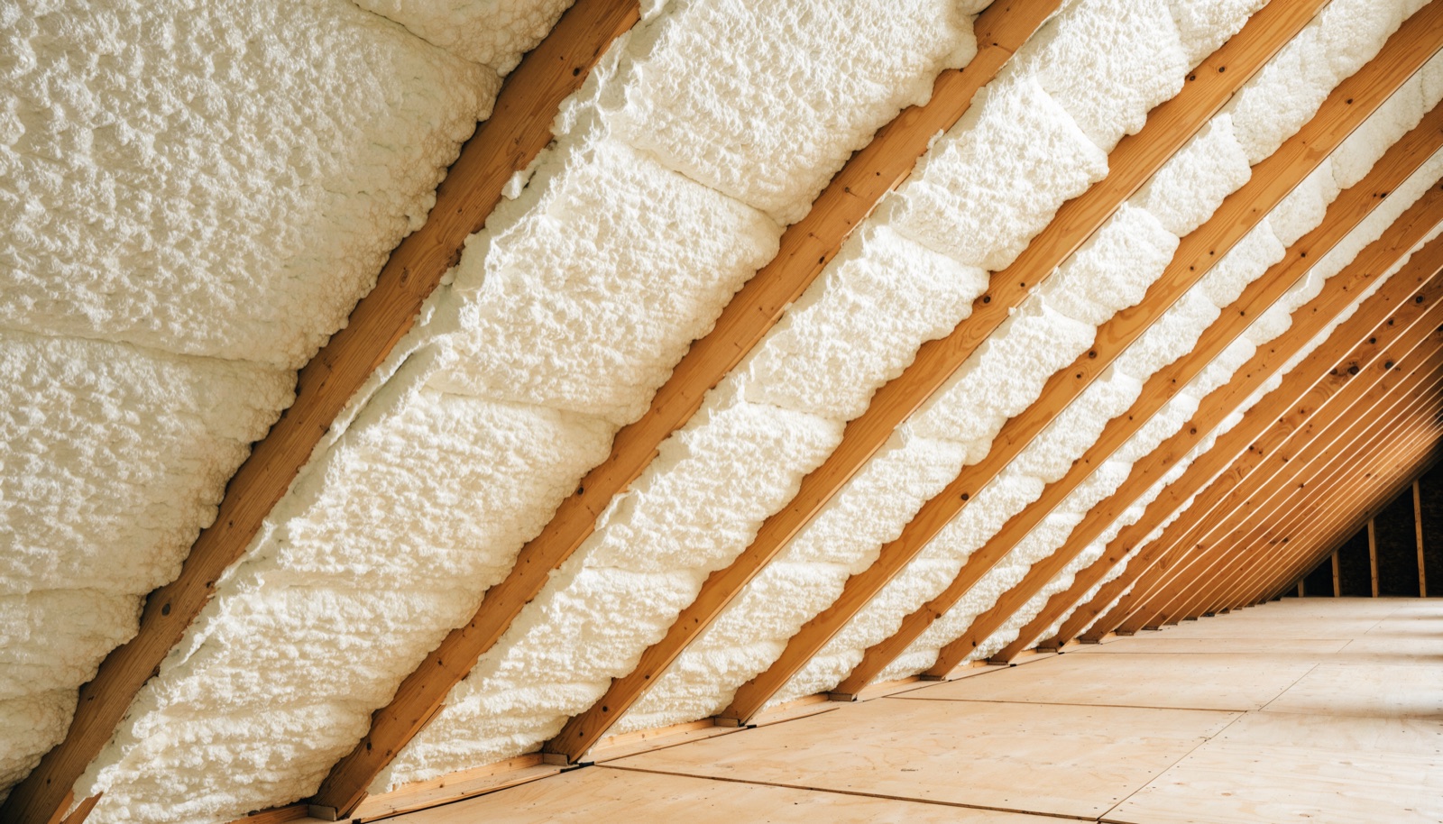 The underside of a residential roof deck insulated with pale expanded spray foam between the rafters, forming a sealed attic